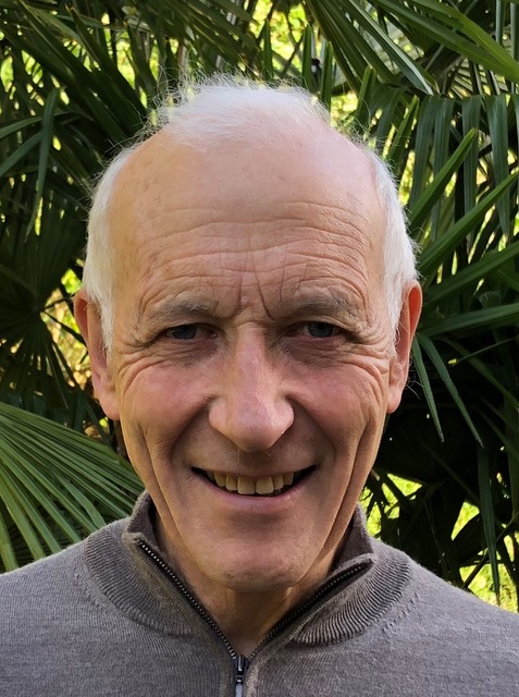 Headshot of Graham. He stands in front of thick greenery and smiles at the camera.