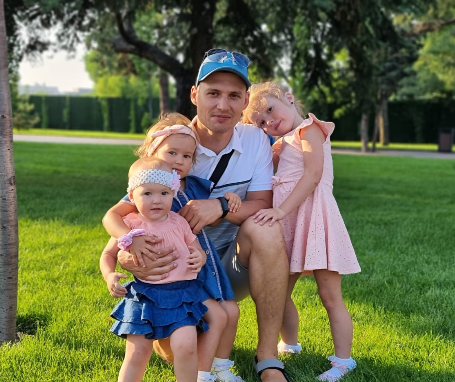 A father hugs his three daughters in a park.