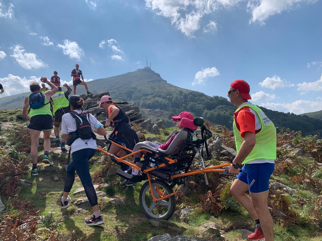 A girl in a chair embarks up a mountain with a team of volunteers.