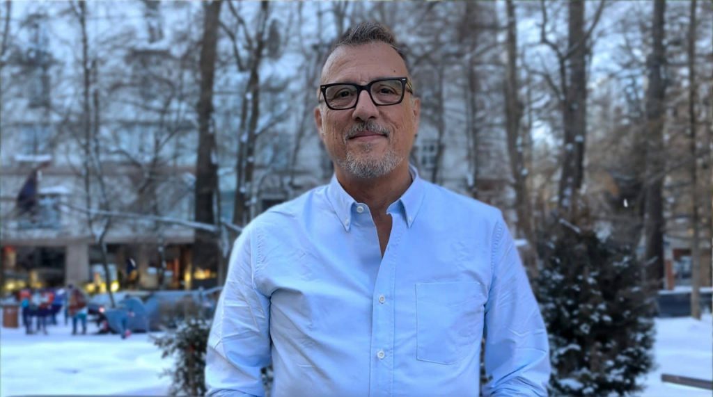 Yann Le Cam stands smiling in a snow-covered park with a blurred café scene behind.