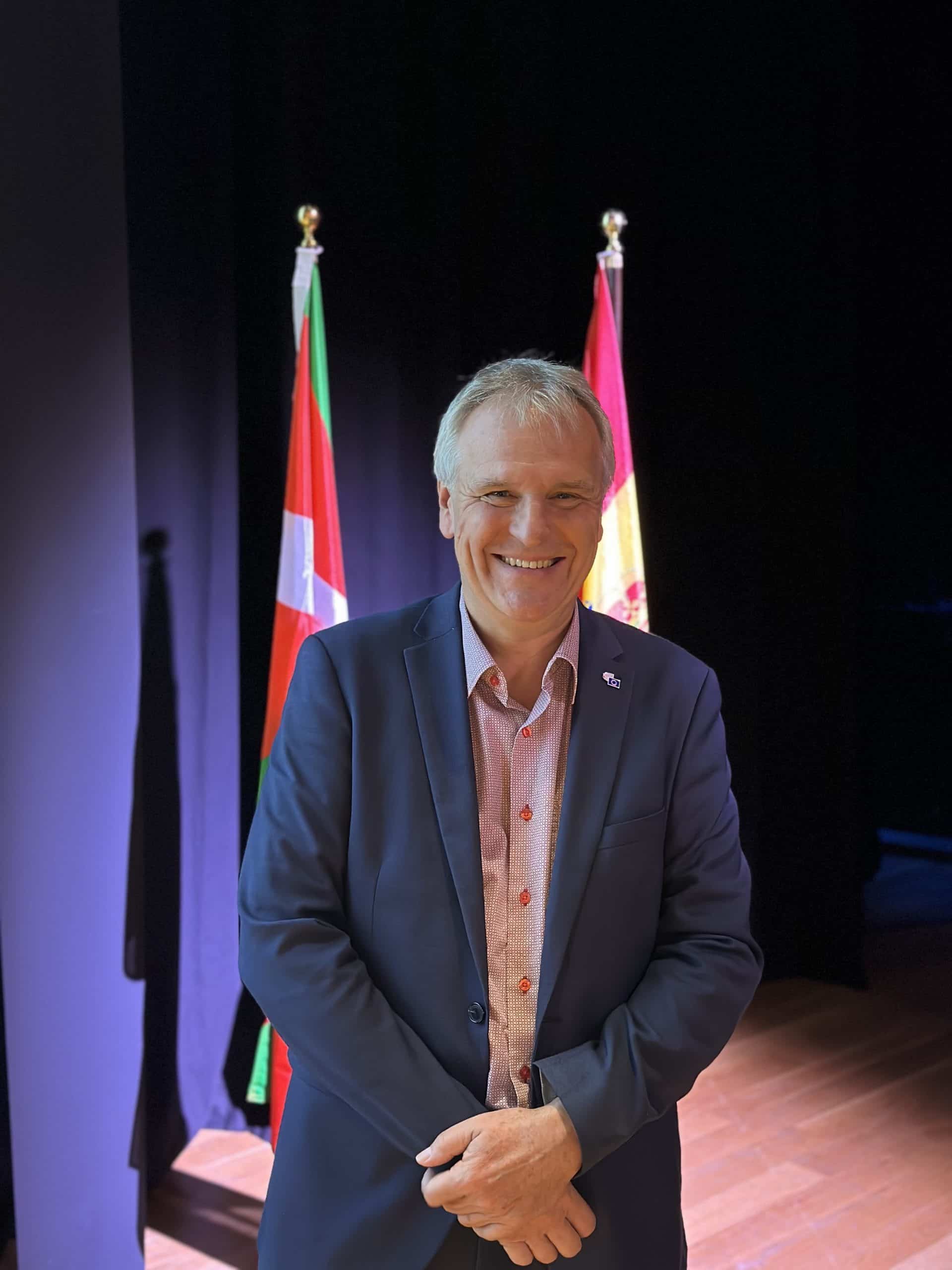 Alain Coheur smiles and stands in front of flags representing EU countries.