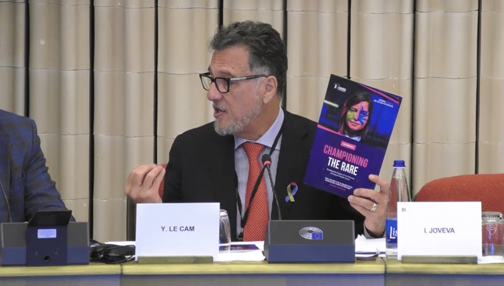 Yann Le Cam, Chief Executive Officer of EURORDIS, holds up the EURORDIS 'Championing the Rare' campaign booklet and gestures while speaking to MEPs.