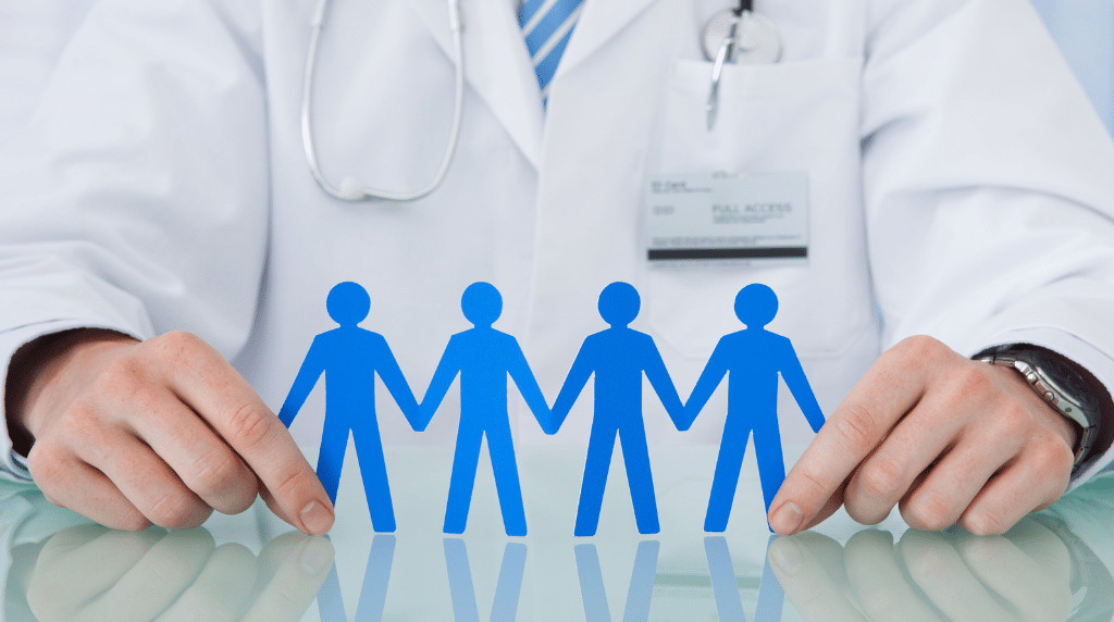 A doctor in a white coat displaying a paper chain of four blue human figures, symbolising patient involvement.