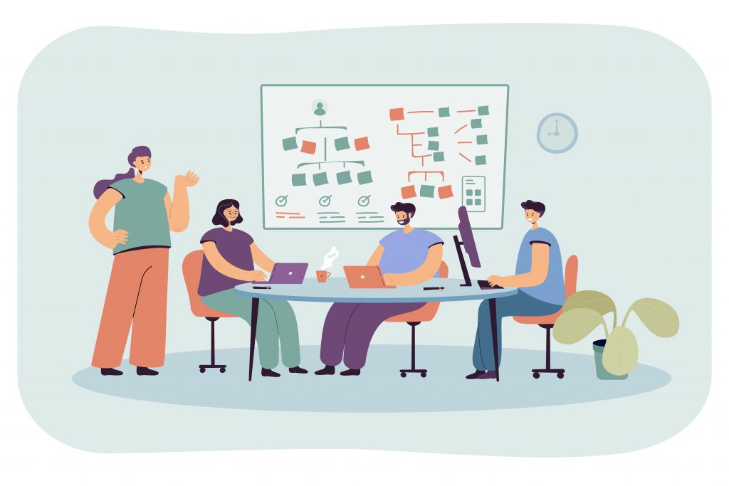 An illustration of a team of four people working in an office setting. Three individuals are seated around a round table with laptops and a desktop computer, while one person stands nearby, gesturing. A whiteboard with a flowchart and sticky notes is displayed in the background. A clock is on the wall, and a potted plant is placed beside the table. The scene conveys teamwork and collaboration in a modern office environment.