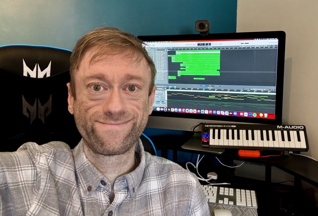 Selfie photo of Leon with the computer he uses to create music with in the background.
